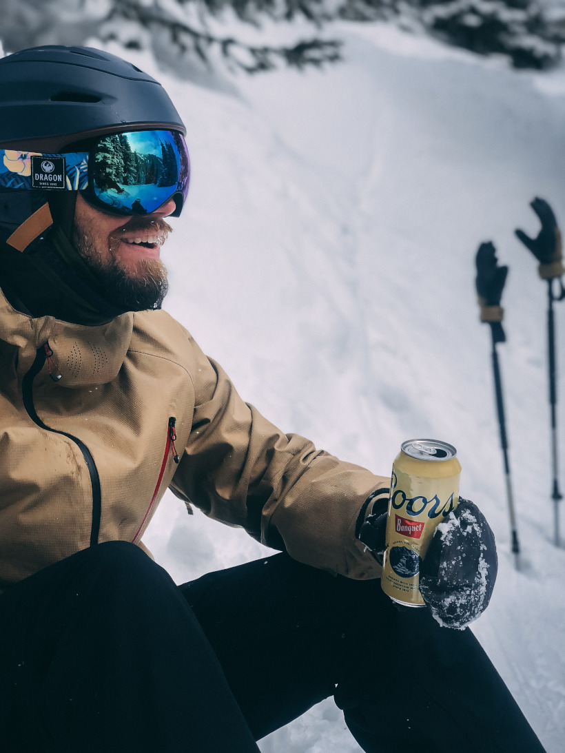 Skier sitting in snow holding beer can